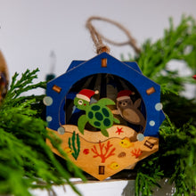 Load image into Gallery viewer, Decorative 3D Christmas ornament with a turtle and monk seal design on a green tree.
