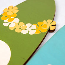 Load image into Gallery viewer, Close up of decorative surfboard with flowers on a green background
